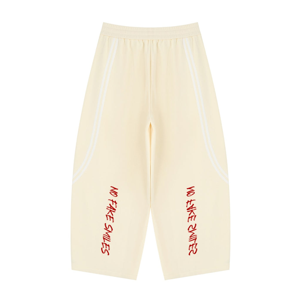 No Fake Smiles wide leg cream sweatpants with white piping detail and red graphic text on the legs.